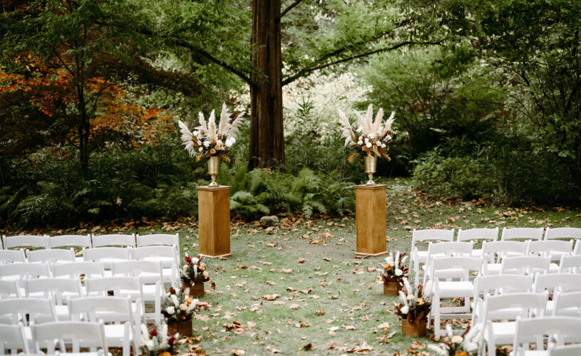 Empty outdoor wedding ceremony with white chairs and two podiums with autumn tone flowers