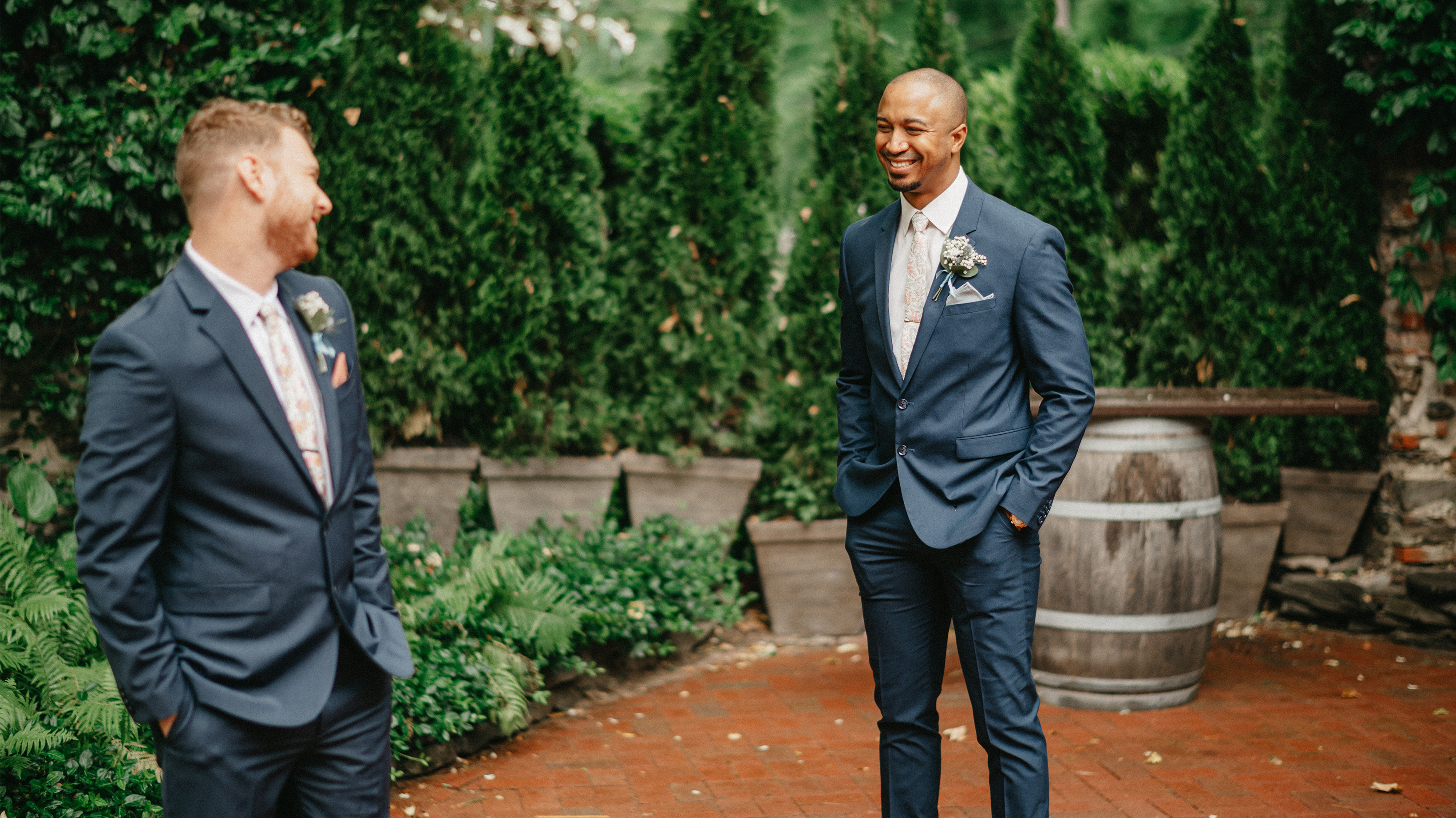 two grooms doing their first look outside in front of lush bushes