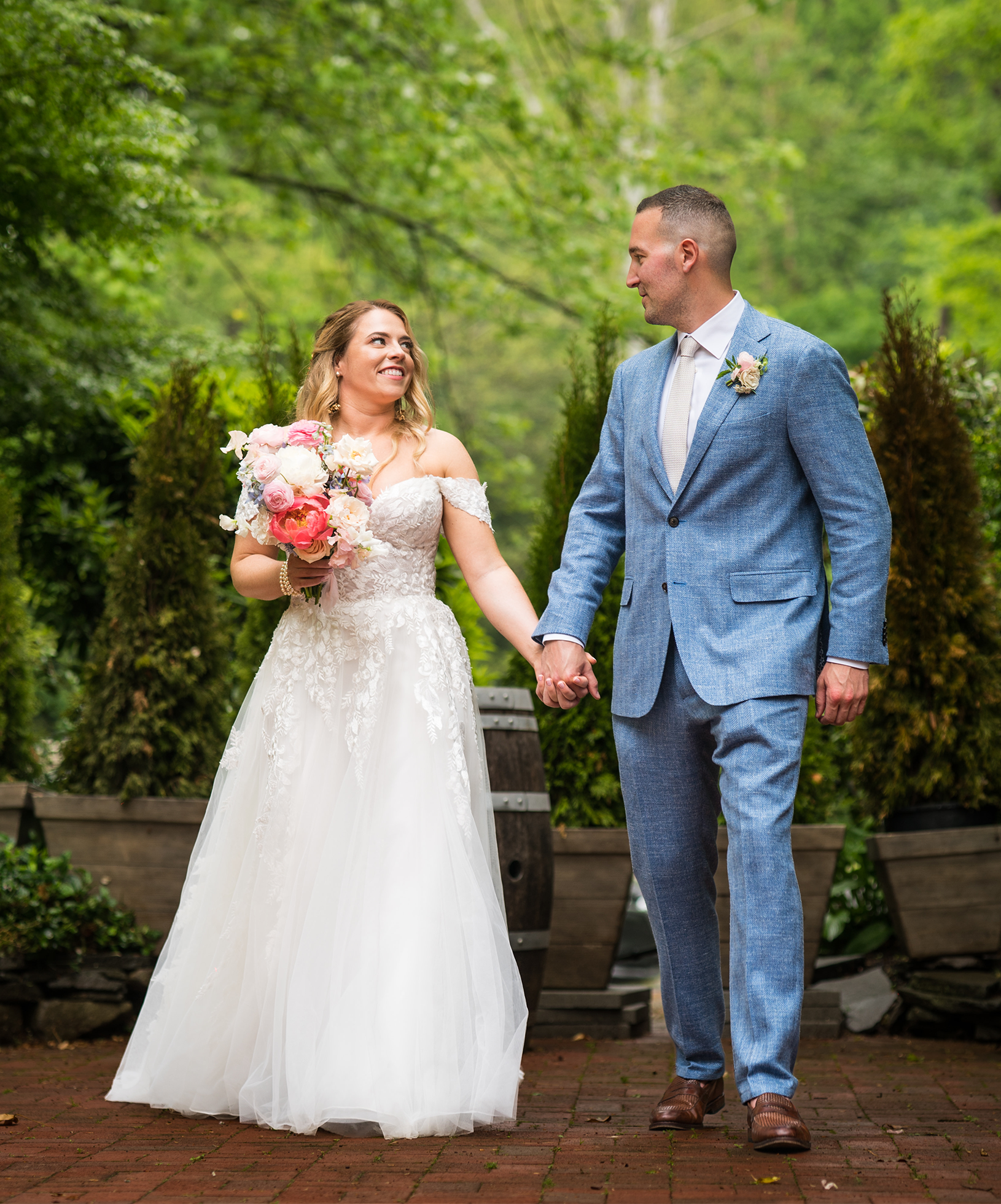 Bride with colorful bouquet holding hands with groom in light blue suit outside.