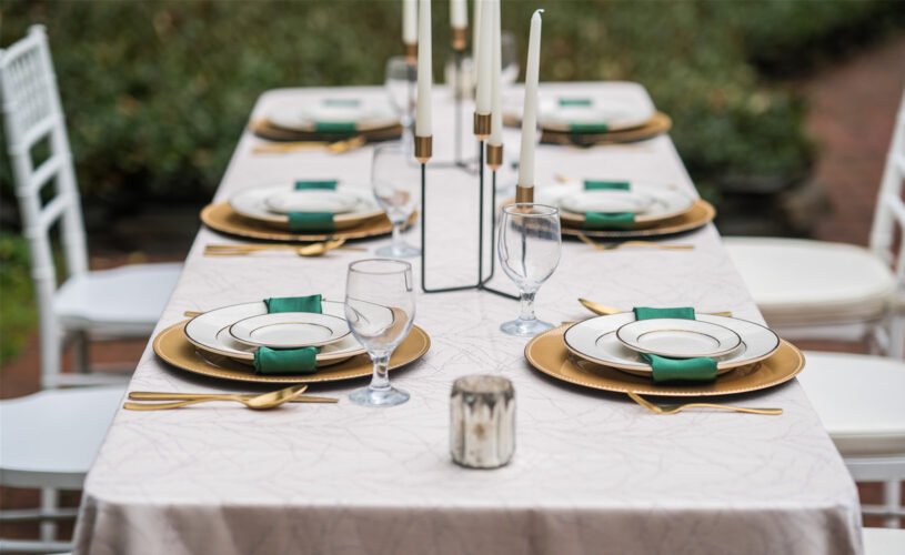 close up of rectangle table with white table cloth and set with gold green and white plate settings.