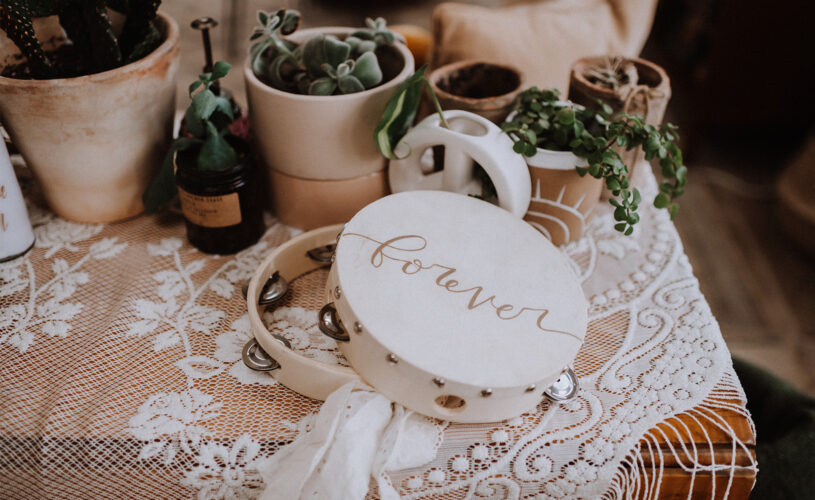 Table with lace tablecloth, plants in clay pots, and a tambourine that says forever.
