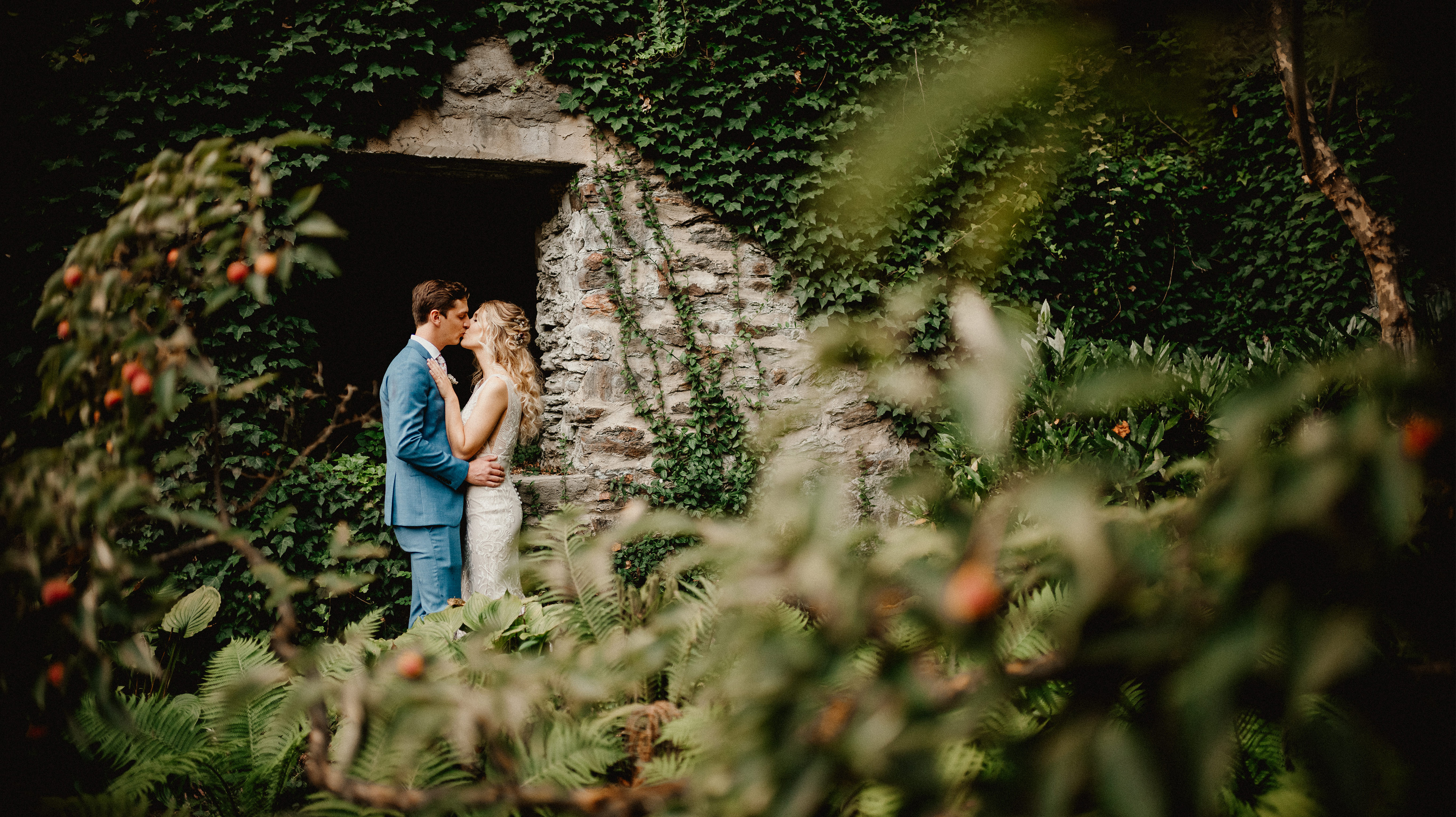 Bride and Groom kissing in outdoor stone doorway covered in vines.