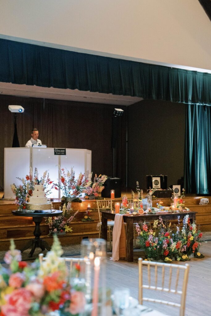 Sweetheart table and cake table with floral in front of a stage.