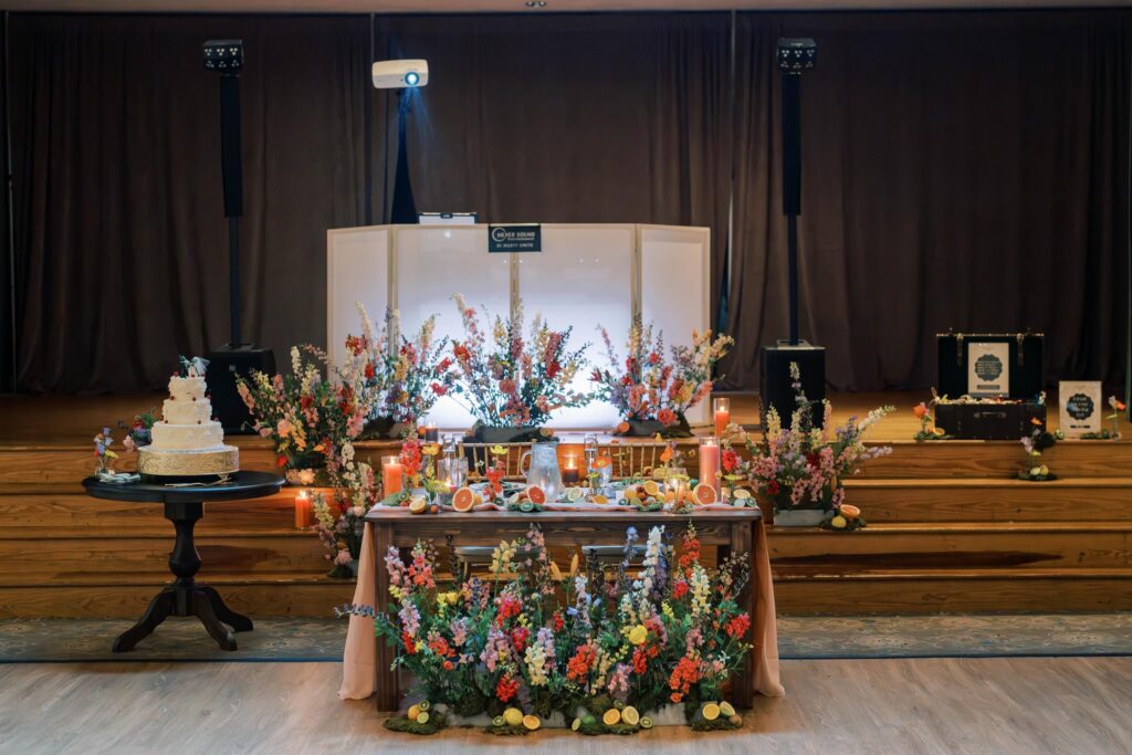 Sweetheart table with floral in front of a stage.